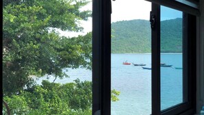 Une vue à travers une fenêtre sur un lac où flottent des bateaux, le tout entouré d’une végétation luxuriante et de collines.