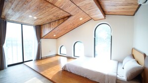 Une chambre avec un plafond en pente, de grandes fenêtres et un plancher en bois.