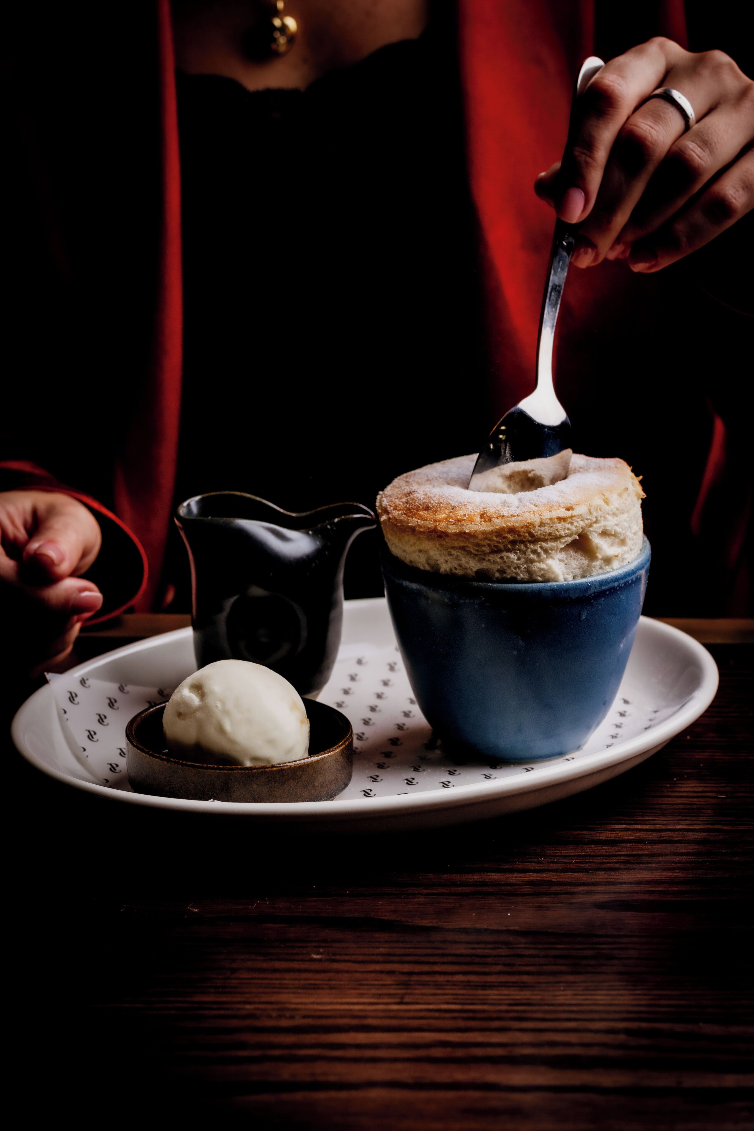 A dessert in a blue cup with a spoon, a small bowl of ice cream, and a black pitcher on a white plate.