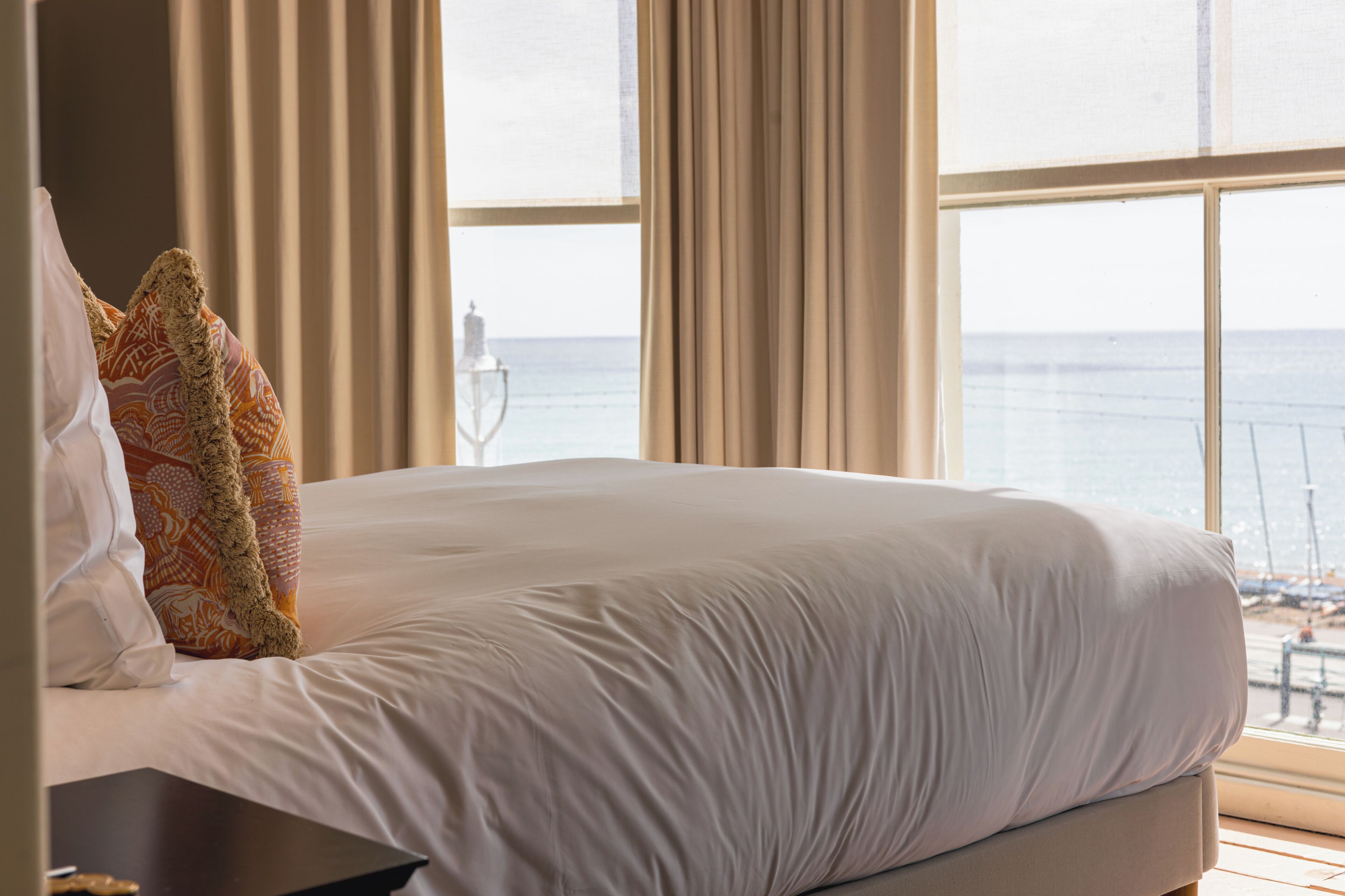 A bed with white linens, a patterned pillow, and a view of the sea through large windows.