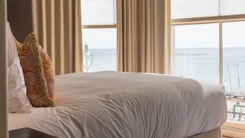 A bed with white linens, a patterned pillow, and a view of the sea through large windows.