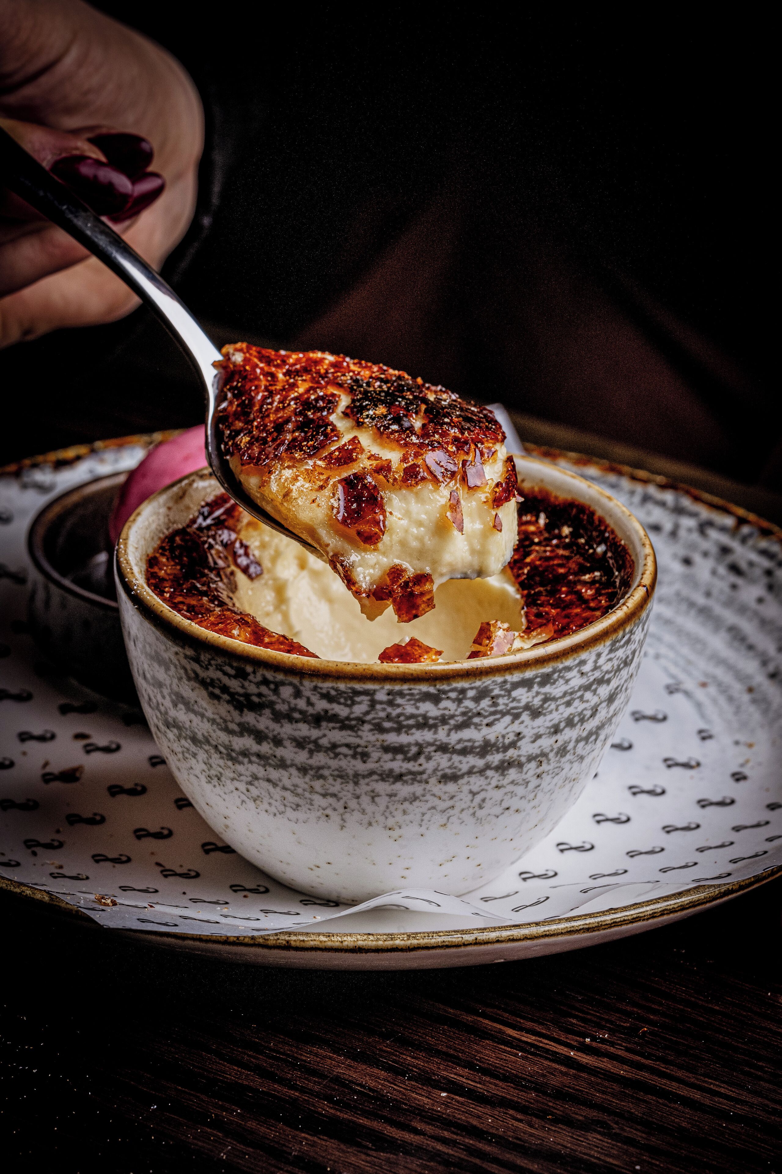 A spoonful of crème brûlée being lifted from a ceramic bowl.