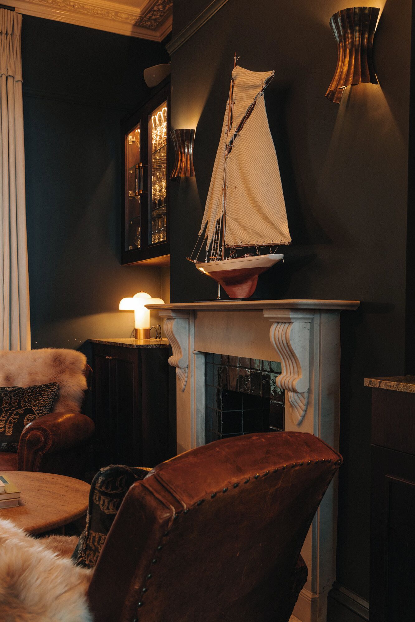 A cozy room with a fireplace, a leather armchair, a lamp, and a decorative sailboat model.
