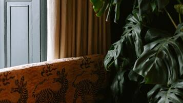 Une pièce avec une fenêtre, un coussin à motifs, une grande plante et une table ronde.