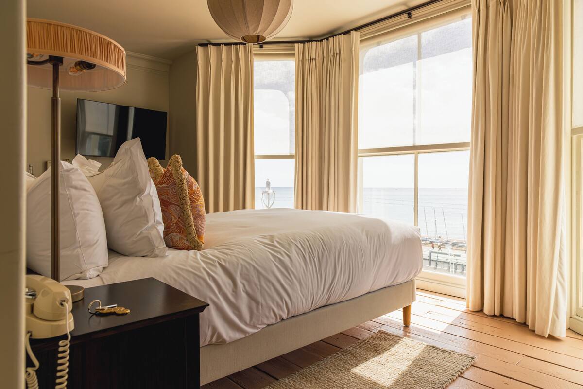 Un dormitorio con cama, mesita de noche con teléfono, lámpara y televisor en la pared.