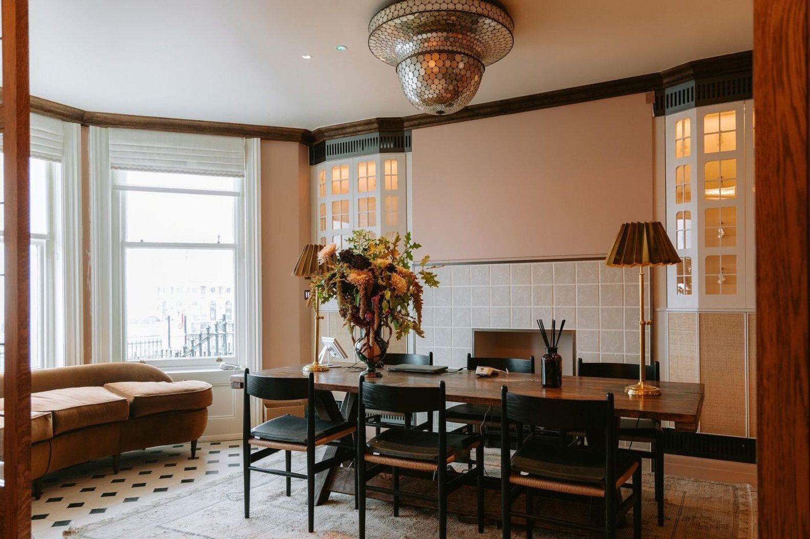 Un espace repas moderne avec une table ronde, des chaises noires, un vase de fleurs, une lampe et une vue sur la ville grâce à de grandes fenêtres.