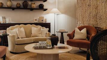 A cozy living room with a beige sofa, a brown armchair, a coffee table, and a bookshelf with decorative items.