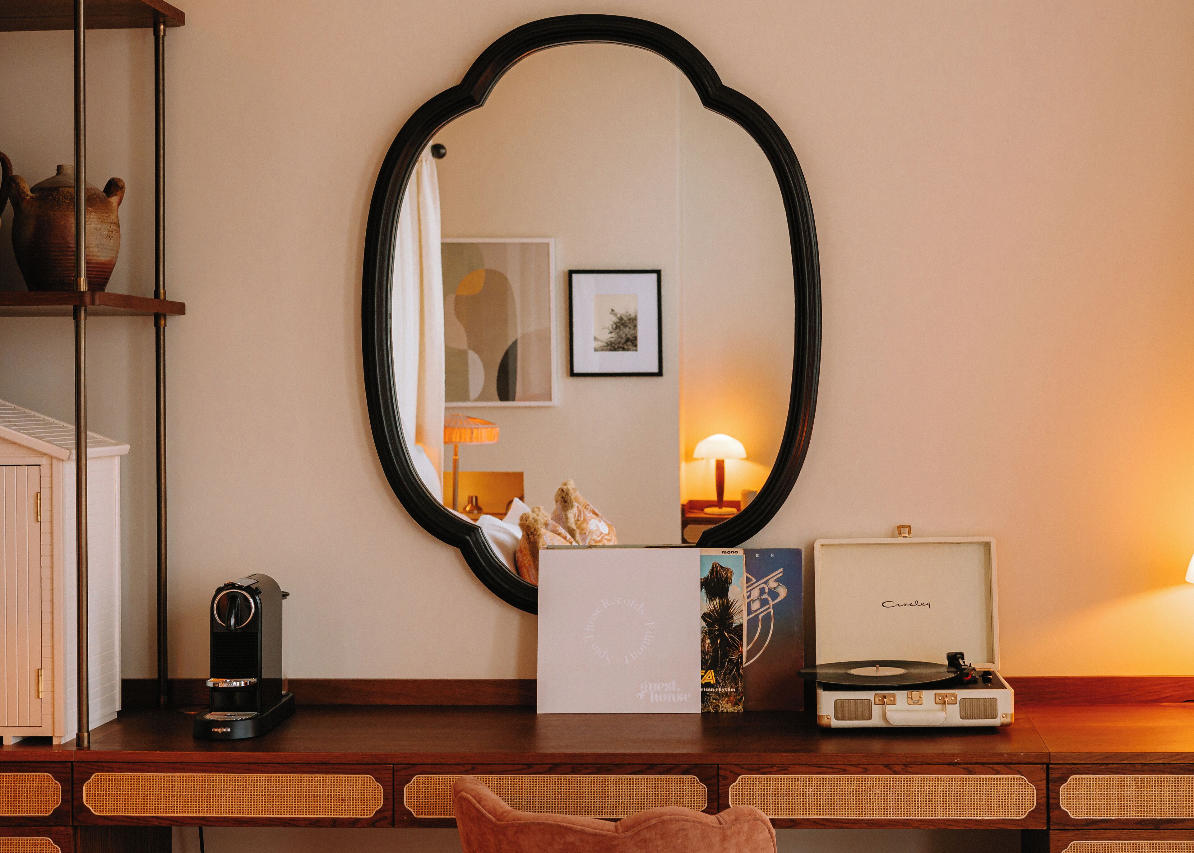 Una habitación con un escritorio de madera, un espejo grande, una cafetera, un tocadiscos y un cuadro en la pared.