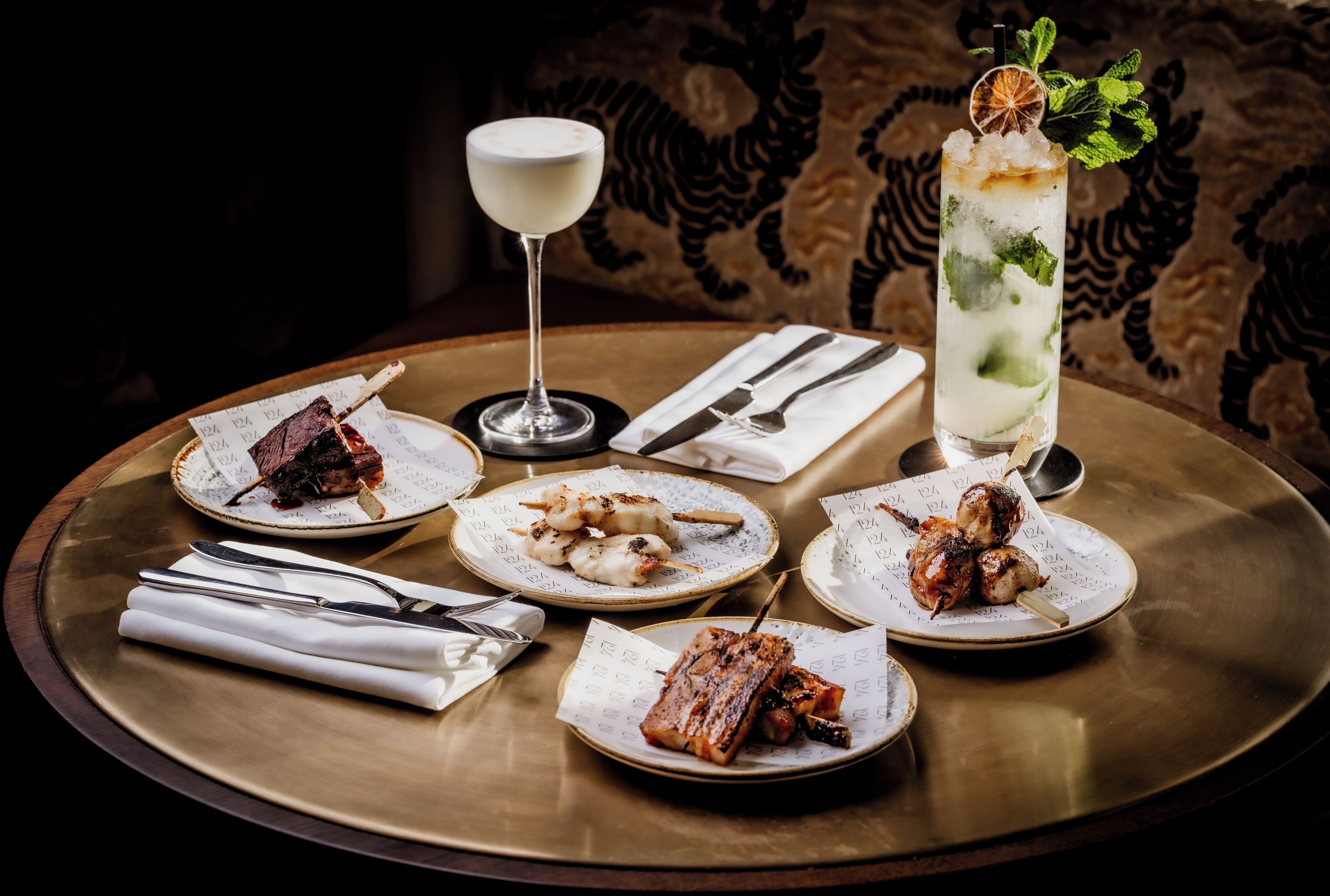 A dining table with plates of food, cutlery, and a tall glass of a beverage.
