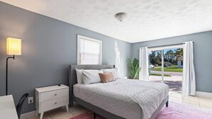 Une chambre à coucher avec un lit, une table de chevet, une lampe, une fenêtre et une vue sur l’extérieur.