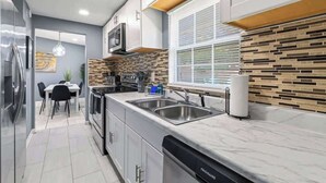 Une cuisine moderne équipée d’appareils électroménagers en acier inoxydable, d’un lave-vaisselle et d’une fenêtre avec des stores.