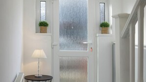 Ein Flur mit einer weißen Tür, einem kleinen Tisch mit einer Lampe und je einer Kübelpflanze auf jeder Seite der Tür.