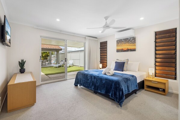 A bedroom with a bed, a nightstand, a wooden cabinet, a ceiling fan, a sliding glass door to a patio, and a painting on the wall. - Seatides Mooloolaba -Pet friendly luxury home with heated pool!! (Sunshine Coast)