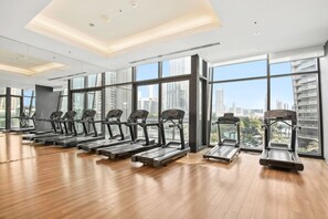 Une salle de sport avec des tapis de course disposés en rangées, de grandes fenêtres et une vue sur le paysage urbain.