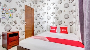 A bedroom with a bed, two red pillows with "OYO" text, a wooden nightstand, and a wall decorated with circular patterns. - Hotel O Bestmela Homestay Syariah (Baturetno)
