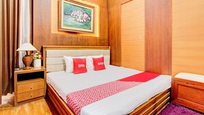 A neatly arranged hotel room with a bed, a nightstand, a lamp, a framed picture, and a clock on the wall. - Hotel O Bestmela Homestay Syariah (Baturetno)