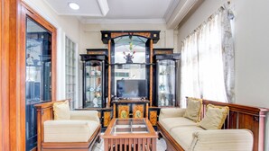 A living room with a wooden coffee table, two sofas, a television, and a cabinet with glass doors. - Hotel O Bestmela Homestay Syariah (Baturetno)