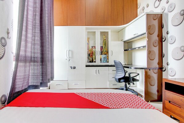 Un dormitorio con cama, escritorio y silla. Se observa un armario con espejo y estante.