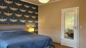 A bedroom with a bed, a nightstand, a lamp, and a door with frosted glass. - Quiet 2 room apartment with WLAN on the first floor - MH5 (Markgrafenheide)