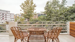 A balcony with wicker furniture, a view of buildings, and a tree. - Treebo Lush Green (Shillong)