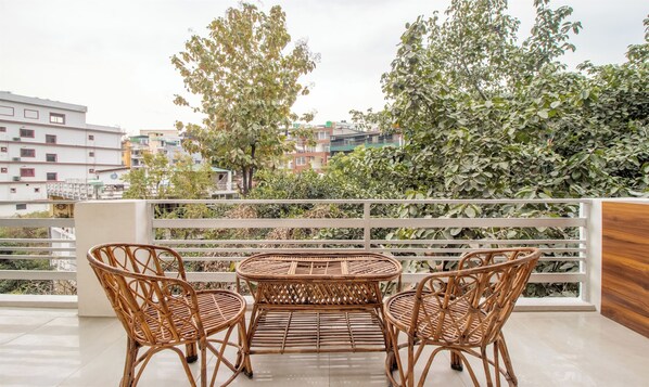 Un balcón con mobiliario de mimbre, vistas a edificios y un árbol.