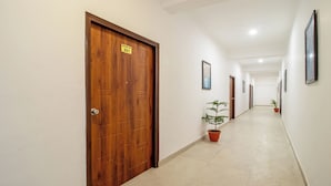 A hallway with wooden doors, numbered room signs, framed artwork on the walls, and potted plants. - Treebo Lush Green (Shillong)
