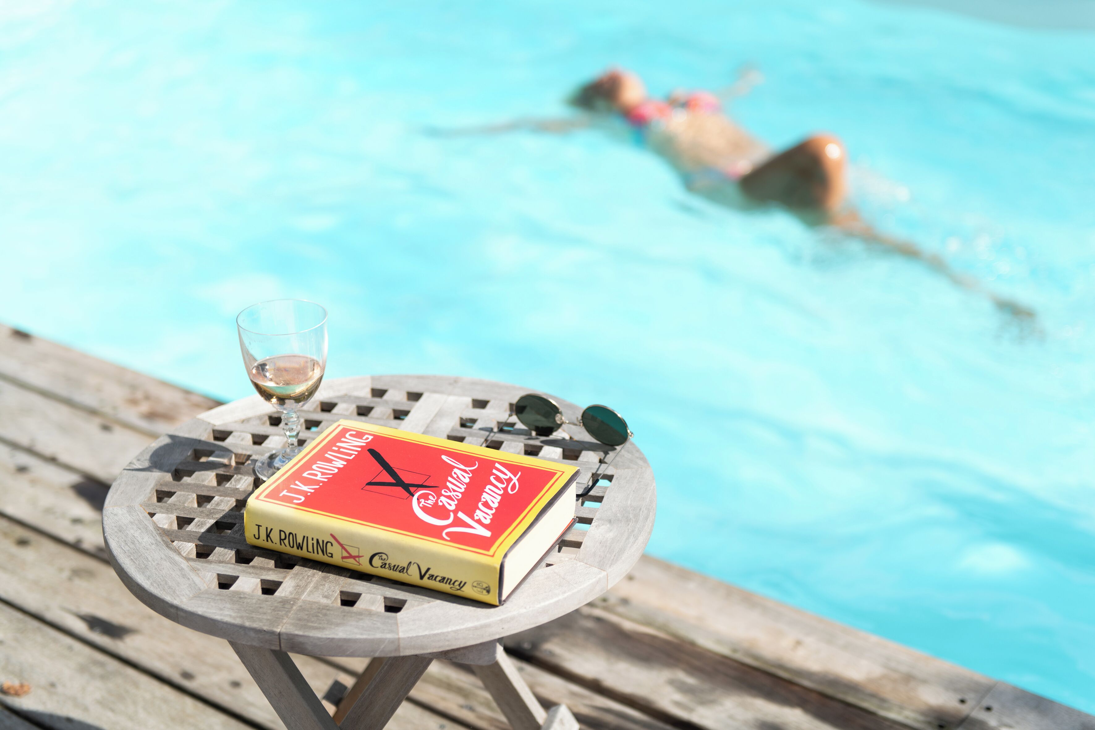 A book titled 'A Casual Vacancy' on a round wooden table by a pool.