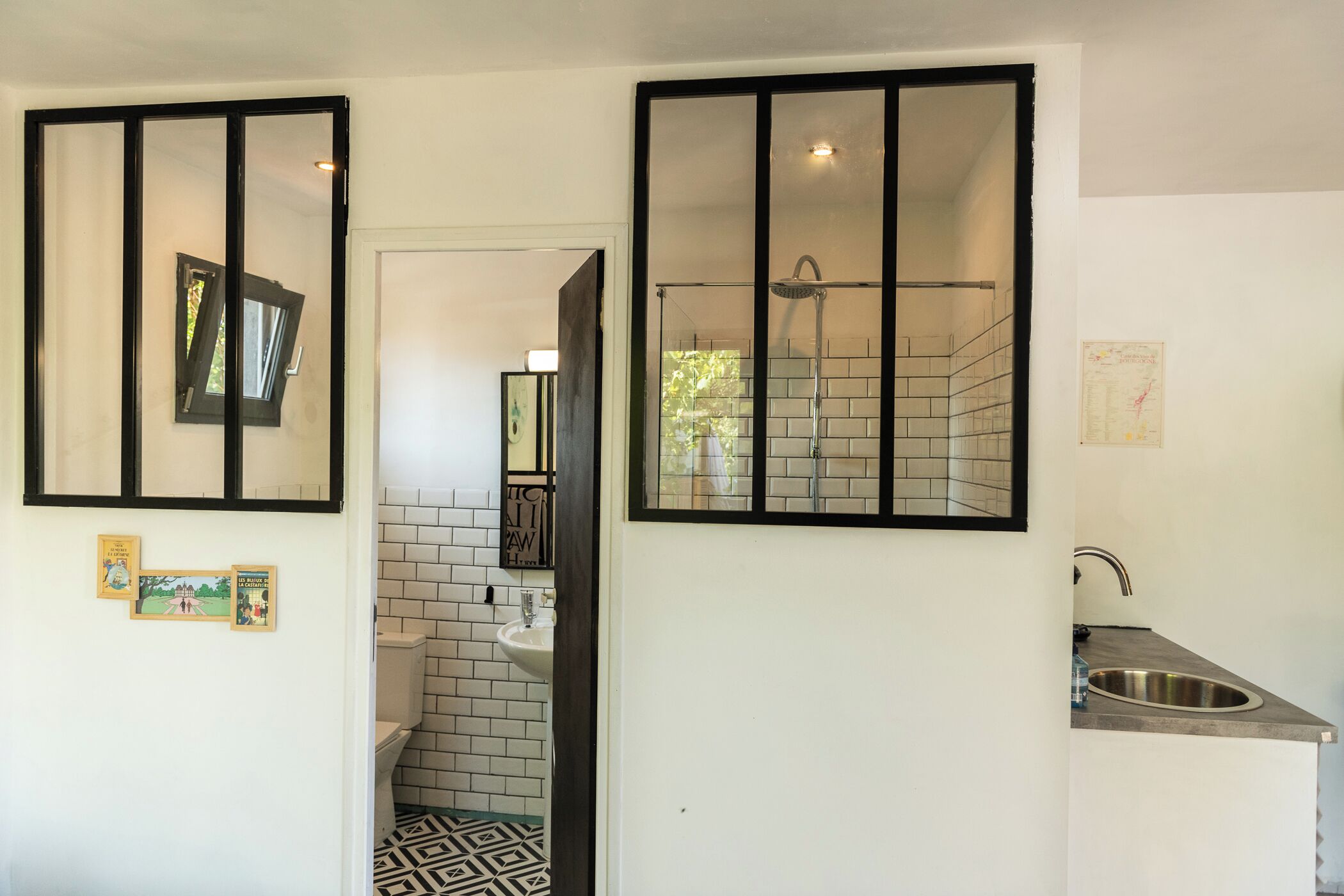 Eine moderne Küche mit Spüle, einem Fenster mit schwarzem Rahmen und einer gefliesten Spritzschutzwand.