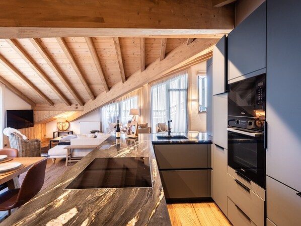 Eine moderne Küche mit Holzbalkendecke, integriertem Herd und einer großen Kochinsel mit Spüle.