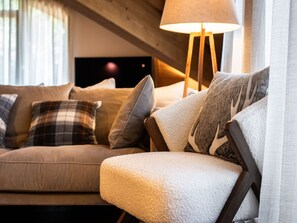 Un salon chaleureux avec un canapé et un fauteuil, une lampe et un téléviseur en arrière-plan.