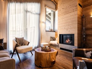 Ein gemütliches Wohnzimmer mit Kamin, Holzwänden und einem großen Fenster mit leichtem Vorhang.
