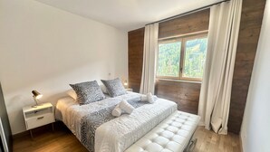 Une chambre moderne avec un grand lit, une table de chevet avec une lampe, un banc et une fenêtre avec des rideaux.