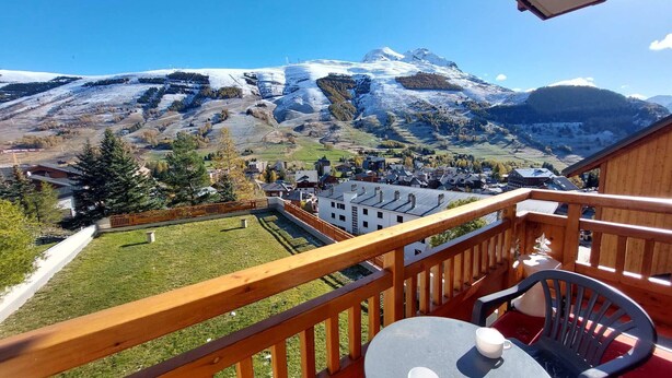 A balcony with a table and chairs, overlooking a village and snow-capped mountains. - T2 Apartment with view, parking, 4 pers in Les Deux Alpes (Les Deux Alpes)
