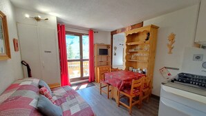 A room with a bed, a dining table with chairs, a kitchen area, and a large window with curtains. - T2 Apartment with view, parking, 4 pers in Les Deux Alpes (Les Deux Alpes)