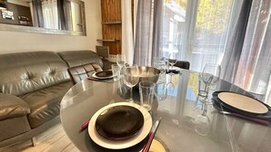 Un salon moderne avec une table à manger en verre pour deux personnes, un canapé en cuir et une étagère en bois.
