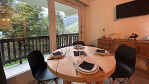 A dining area with a round table set for four, chairs, a wooden cabinet, and a TV mounted on the wall. - Ski-in/Ski-out studio, 3 ppl, Méribel center, balcony, TV, fiber (Méribel)