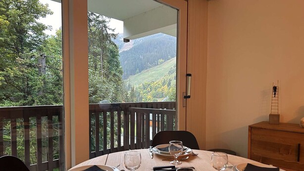 A dining table set for four with a scenic mountain view through a large window. - Ski-in/Ski-out studio, 3 ppl, Méribel center, balcony, TV, fiber (Méribel)