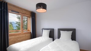 Ein Zimmer mit zwei Betten, einem großen Fenster mit Vorhängen und einer Hängeleuchte.