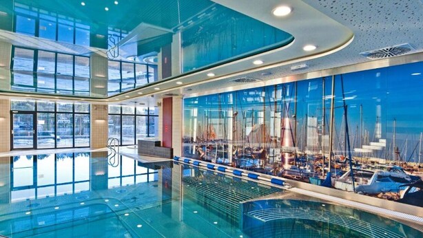 Une vaste piscine intérieure dotée d’un mur de verre qui reflète le paysage d’une marina.