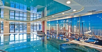 Una amplia piscina interior con un muro de cristal que refleja una vista de la marina.
