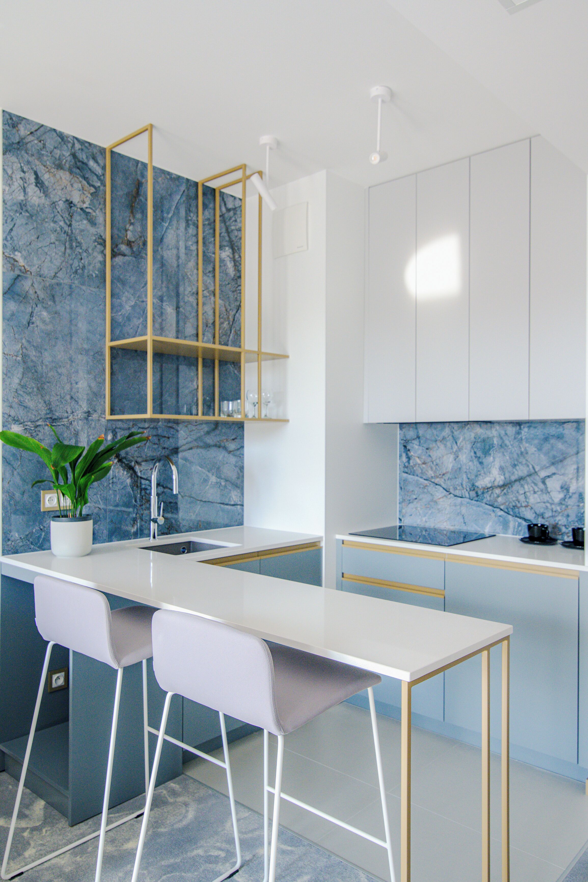 Una cocina moderna con salpicadero de mármol, armarios blancos y una isla central con taburetes de bar.