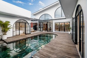 Ein moderner Poolbereich im Freien mit Holzterrasse, Glaswänden und freiem Blick ins Innere.