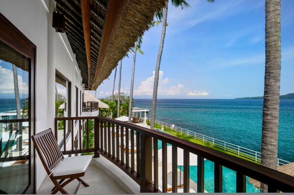 A balcony with a view of the ocean, palm trees, and a thatched roof. - Villa Blanca by Alfred in Bali - Modern Luxury 5 Bdr Oceanfront Villa in Candidasa (Manggis)