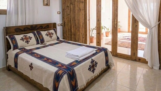 A bedroom with a wooden bed, white curtains, and a view through a glass door.