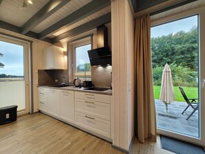A modern kitchen with wooden cabinets, a black range hood, and a large window overlooking a garden.