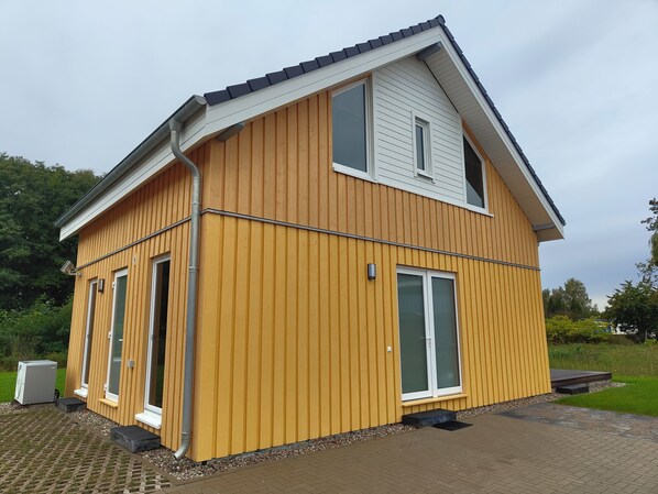 A two-story wooden house with a sloped roof, large windows, and a small porch.