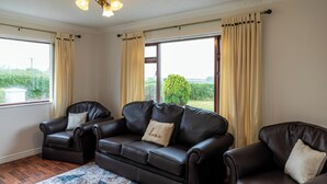 Ein Wohnzimmer mit einem braunen Ledersofa, zwei Sesseln und einem großen Fenster mit Vorhängen.