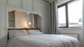 Ein Schlafzimmer mit Bett, Einbauschränken, einer Nachttischlampe und einem Fenster mit Vorhängen.