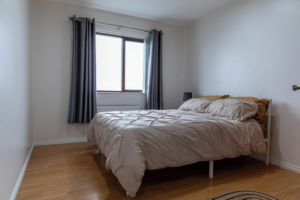 Un dormitori amb llit, finestra amb cortines i radiador.