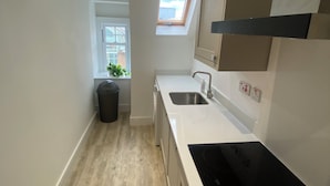 A narrow kitchen with a skylight, a black induction cooktop, and a window with a view of buildings. - Central Paisley Apartment- Airport/glasgow Access (Paisley)